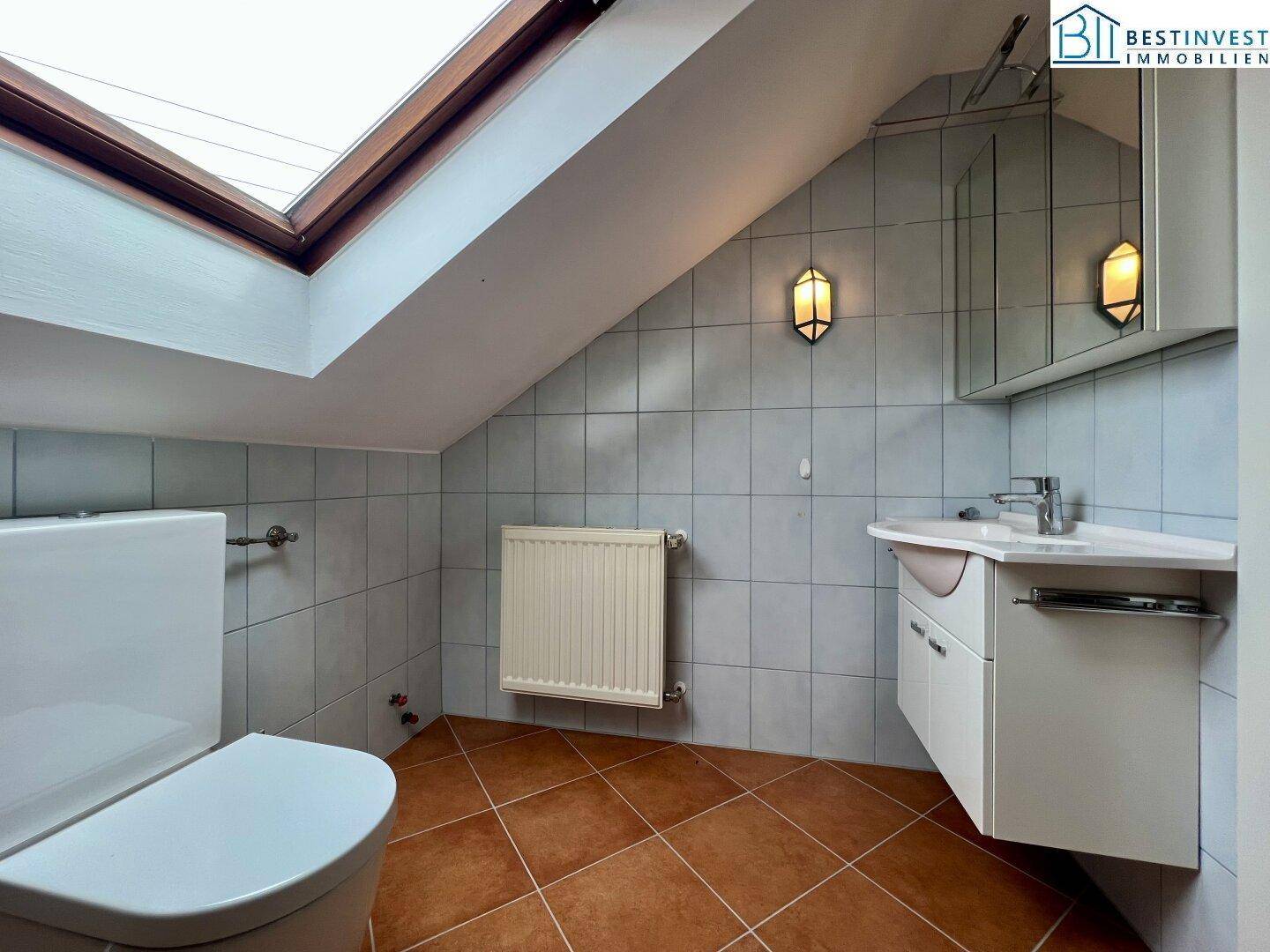 Helles Badezimmer im Dachgeschoss mit Waschbecken, WC und großem Dachfenster für natürliche Belichtung.