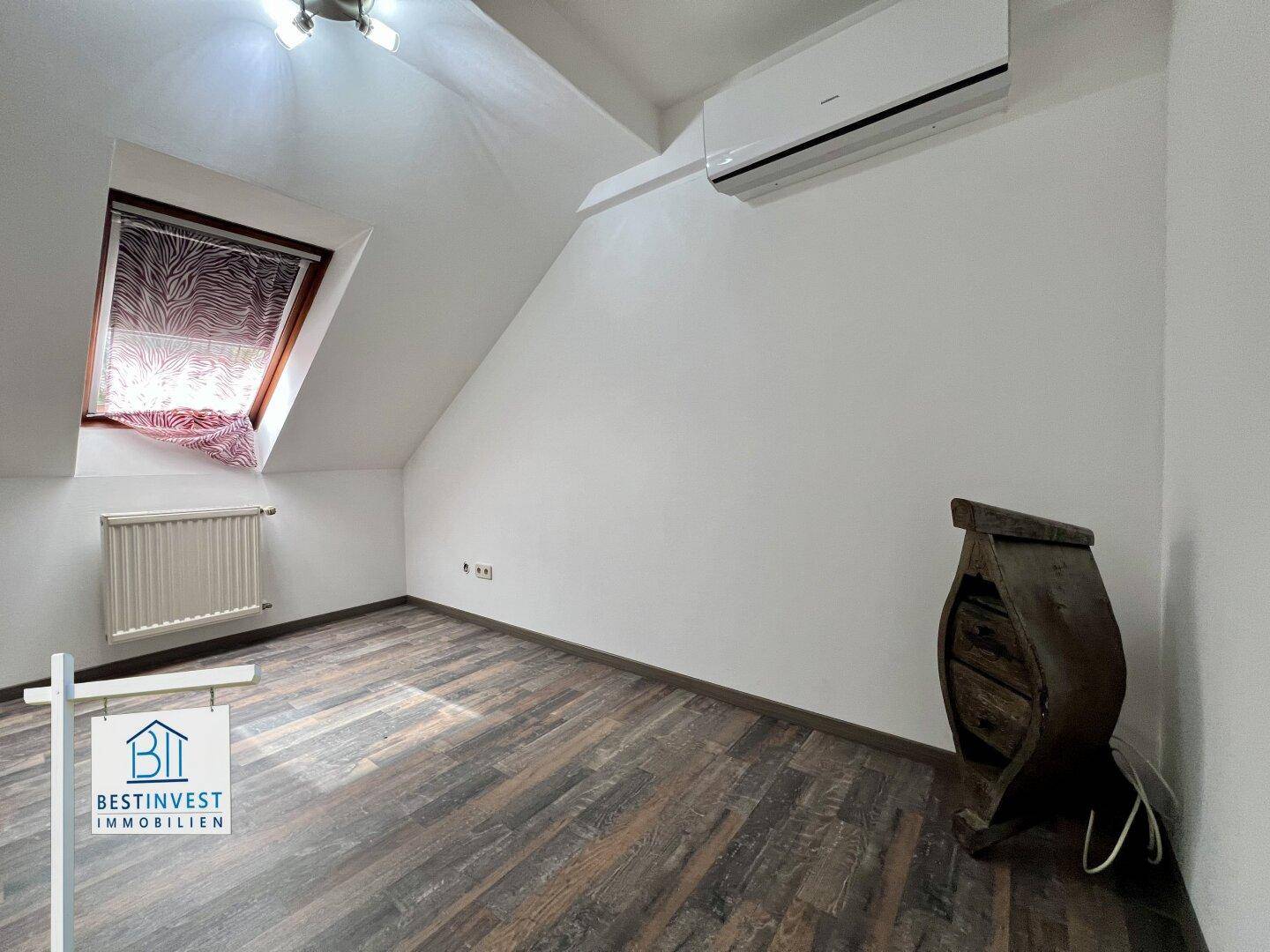 Helles Zimmer mit Dachschrägen, Dachfenster, Klimaanlage und dunklem Laminatboden.