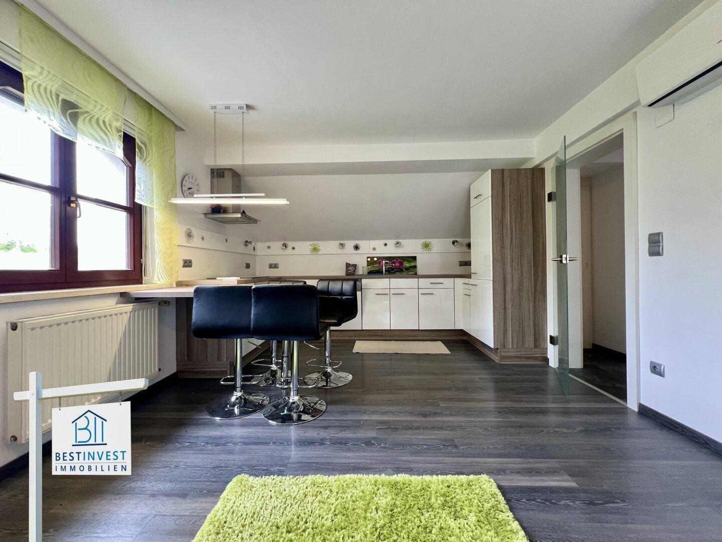 Heller Wohnbereich mit moderner Küchenzeile, Fenster und Klimaanlage in der Dachgeschosswohnung.