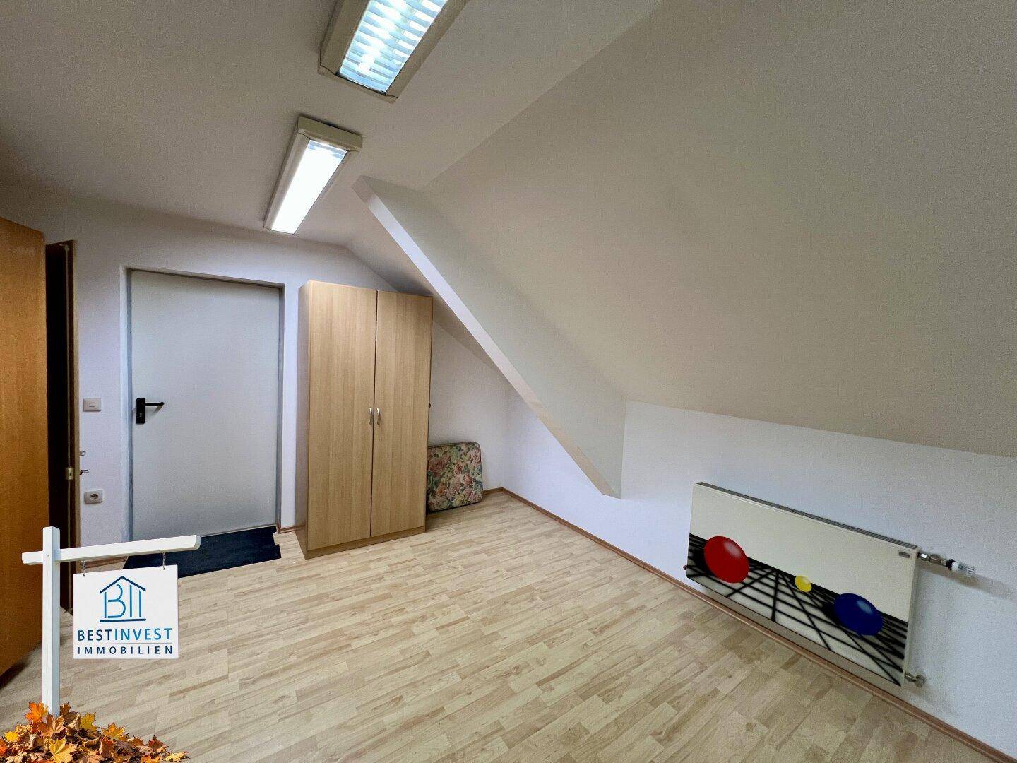 Dachgeschosszimmer mit Dachschrägen, hellem Holzboden und einem farbig gestalteten Heizkörper.