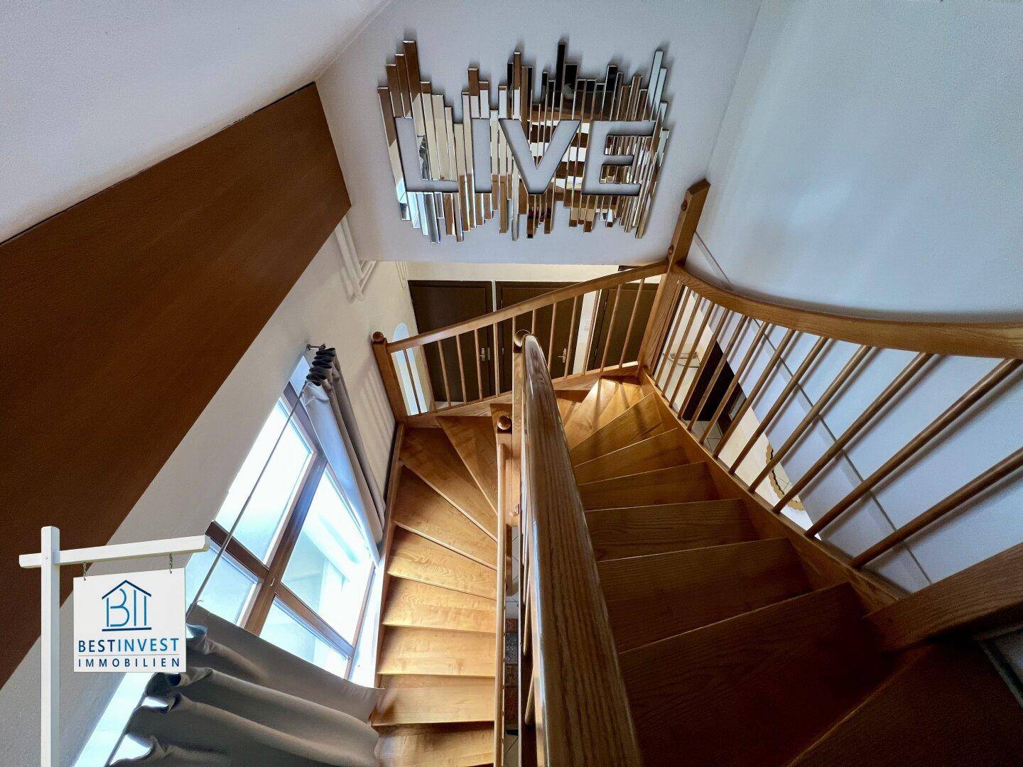 Holztreppe führt in die obere Etage, beleuchtet durch Fenster und mit dekorativem Schriftzug.