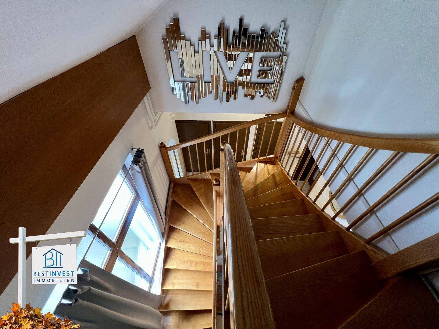 Holztreppe führt in die obere Etage, mit dekorativem Wandspiegel und natürlichem Lichteinfall.
