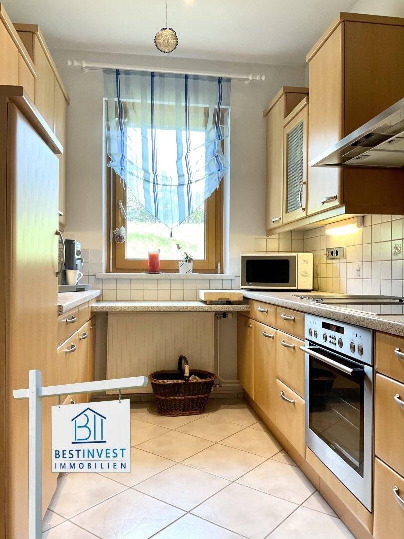 Funktionale Küche mit hellen Holzschränken, Fliesenboden und Fenster mit Ausblick.