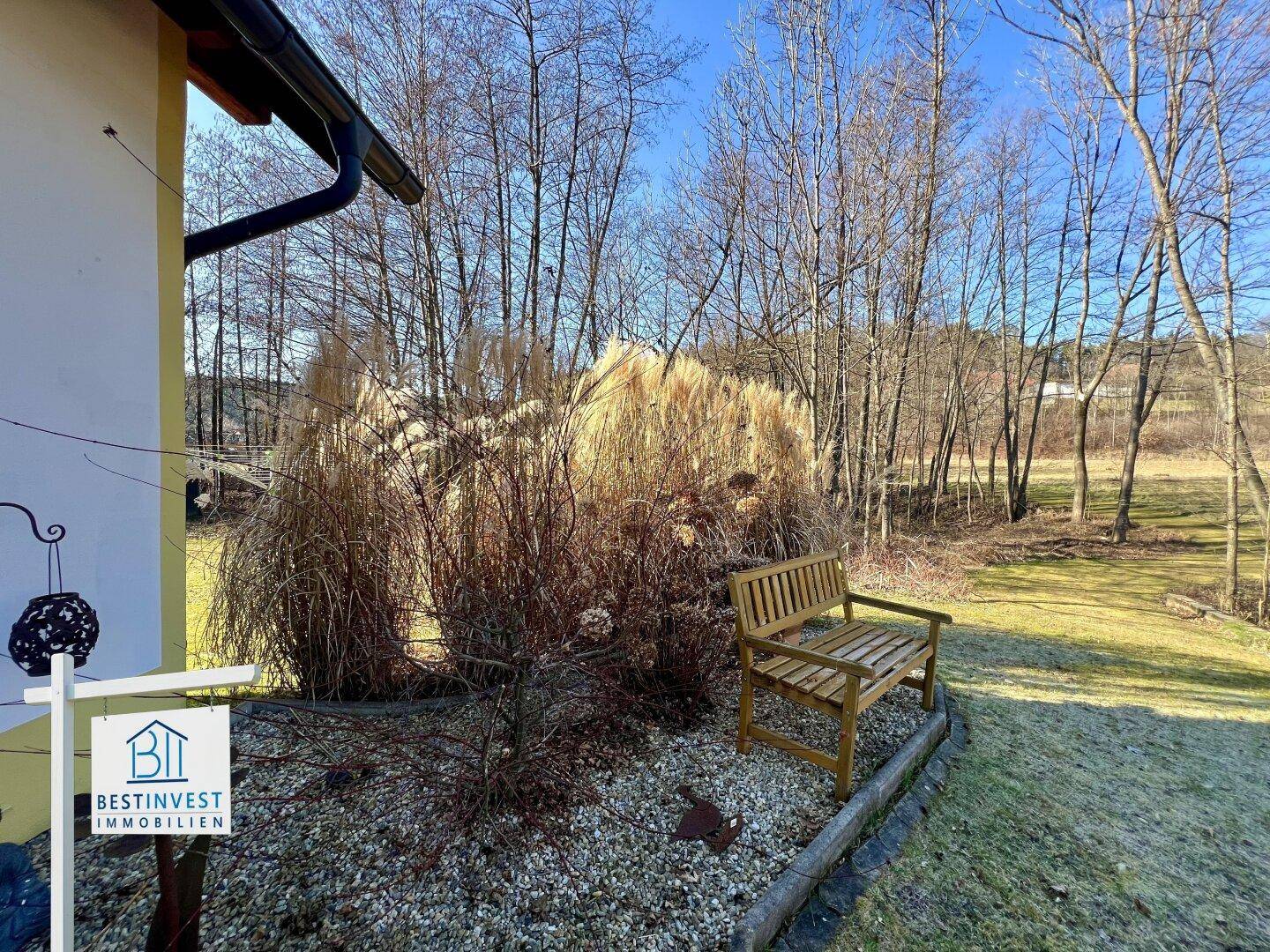 Gemütlicher Gartenbereich mit Holzbank und Ziergräsern, ideal zum Entspannen im Freien.