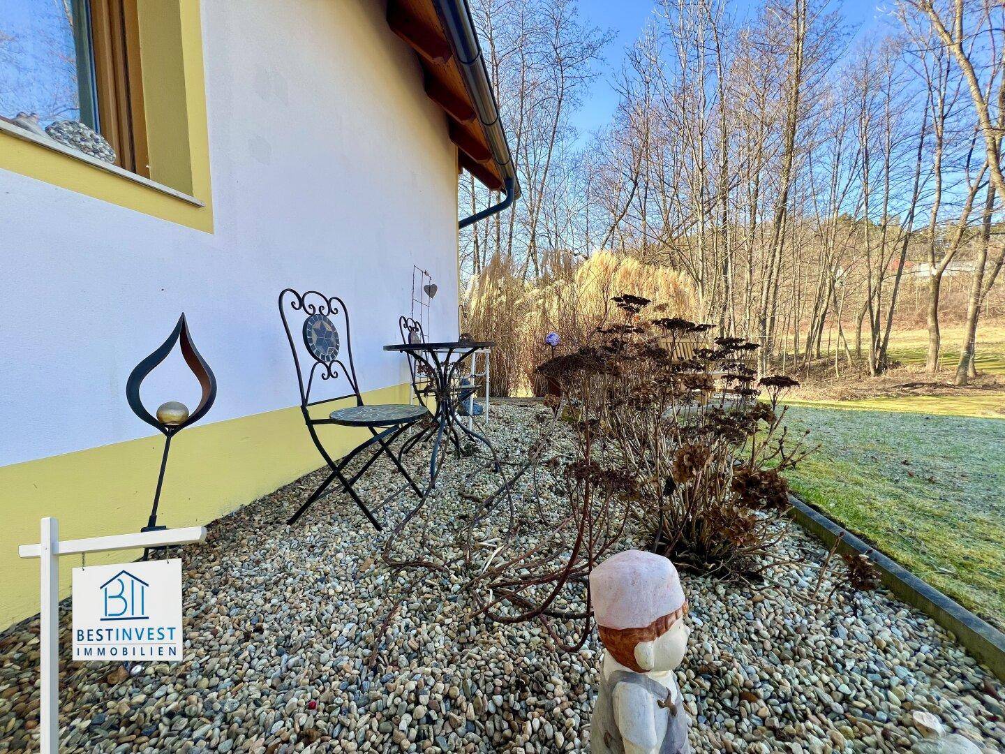 Kleiner Sitzbereich im Garten mit schmiedeeisernen Möbeln und Zierpflanzen auf Kiesuntergrund.