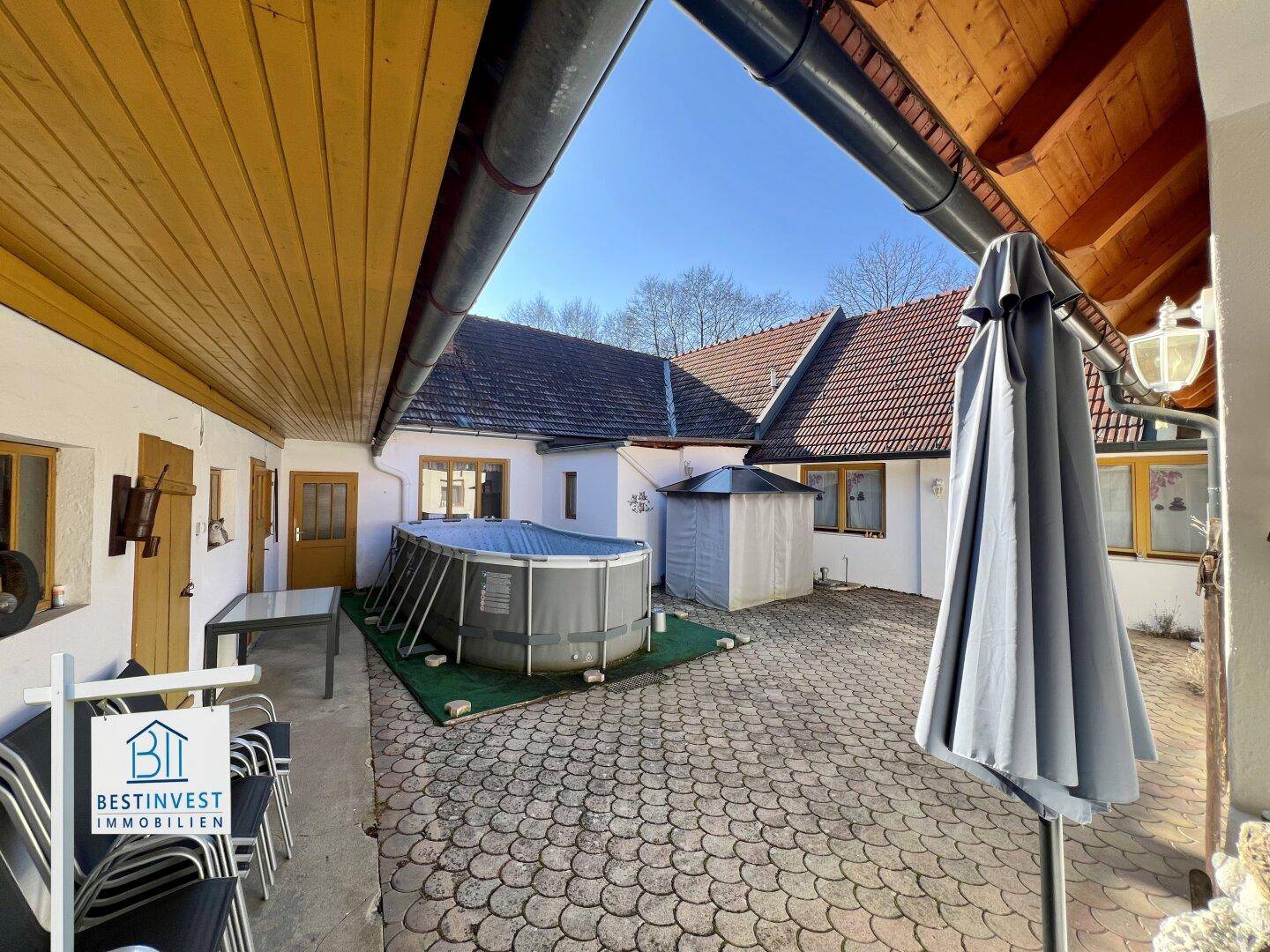 Überdachter Bereich mit Blick auf den gepflasterten Innenhof und den Aufstellpool.