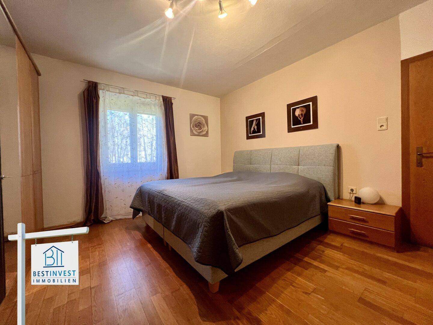 Gemütliches Schlafzimmer mit Doppelbett, Holzparkett und einem Fenster mit Blick ins Grüne.