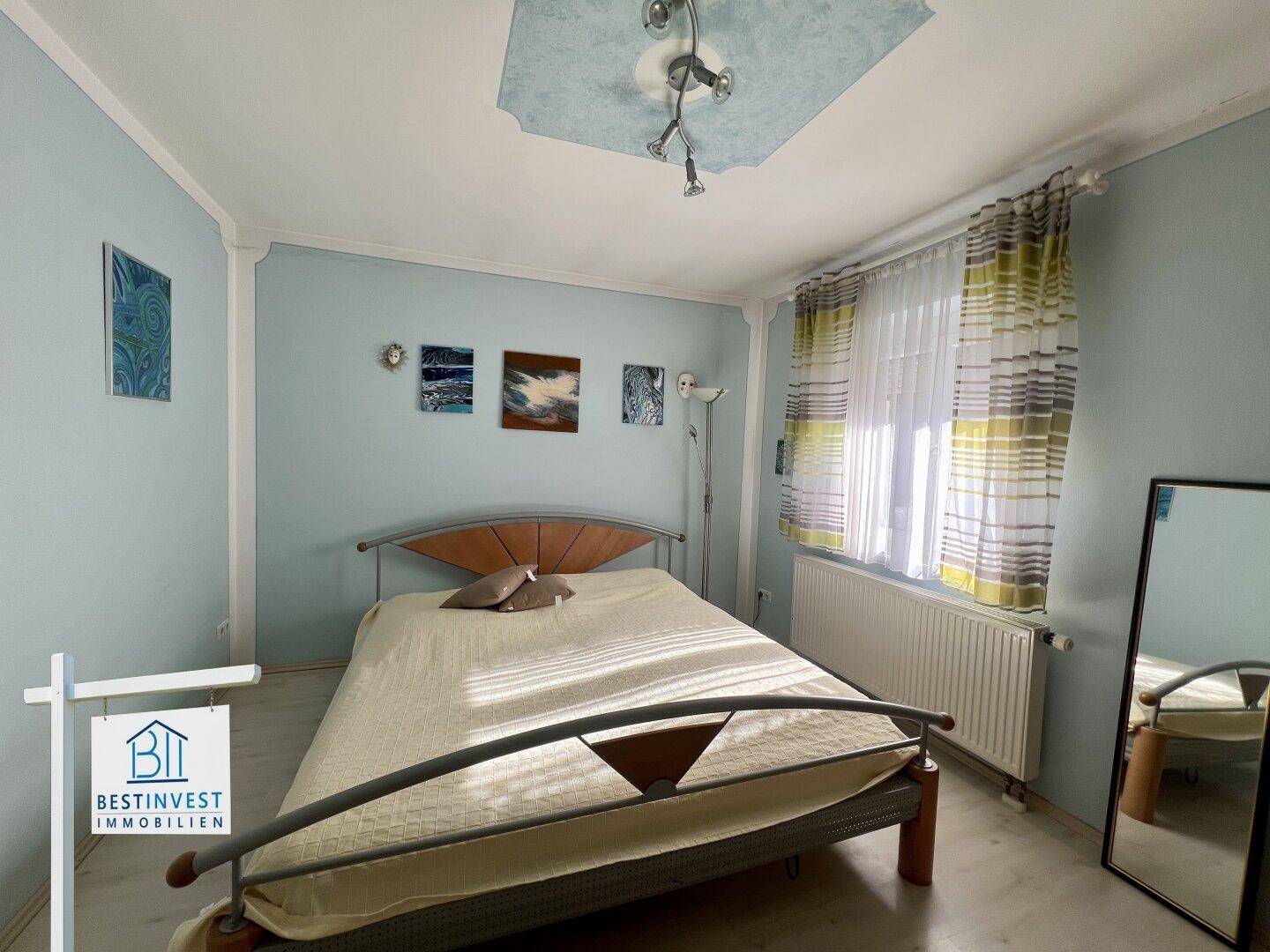 Helles Schlafzimmer mit hellblauen Wänden, einem Doppelbett und einem Deckenlicht.