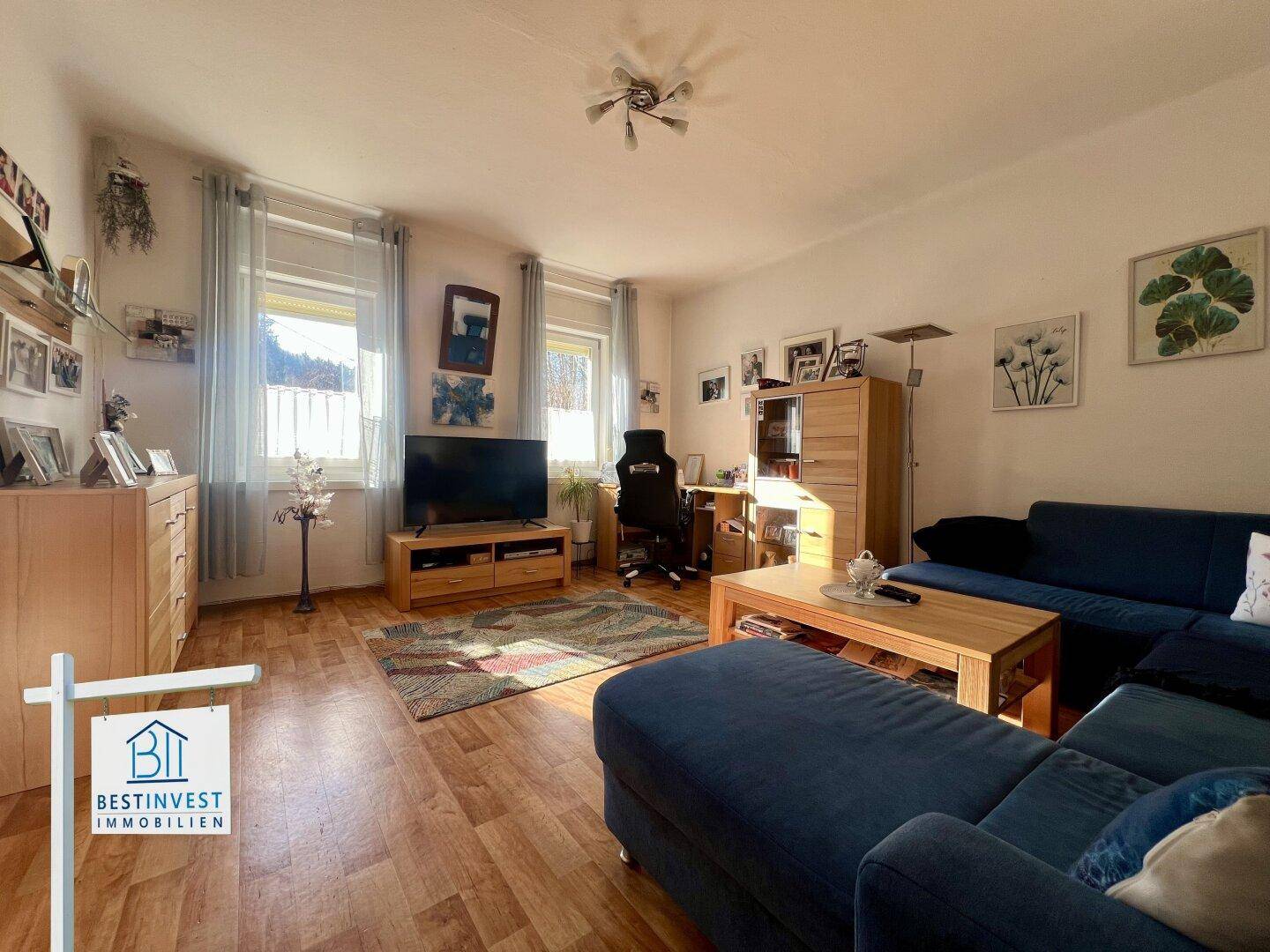 Helles Wohnzimmer mit blauem Sofa, Fernseher und Laminatboden.