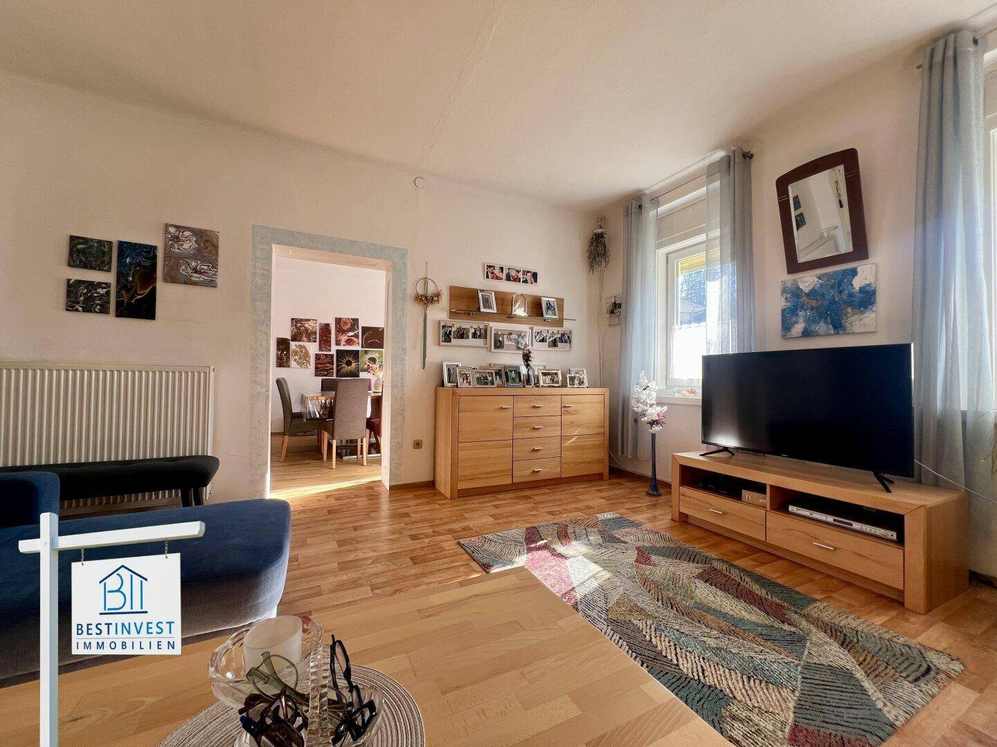 Wohnzimmer mit hellem Laminatboden und offenem Zugang zum Essbereich.
