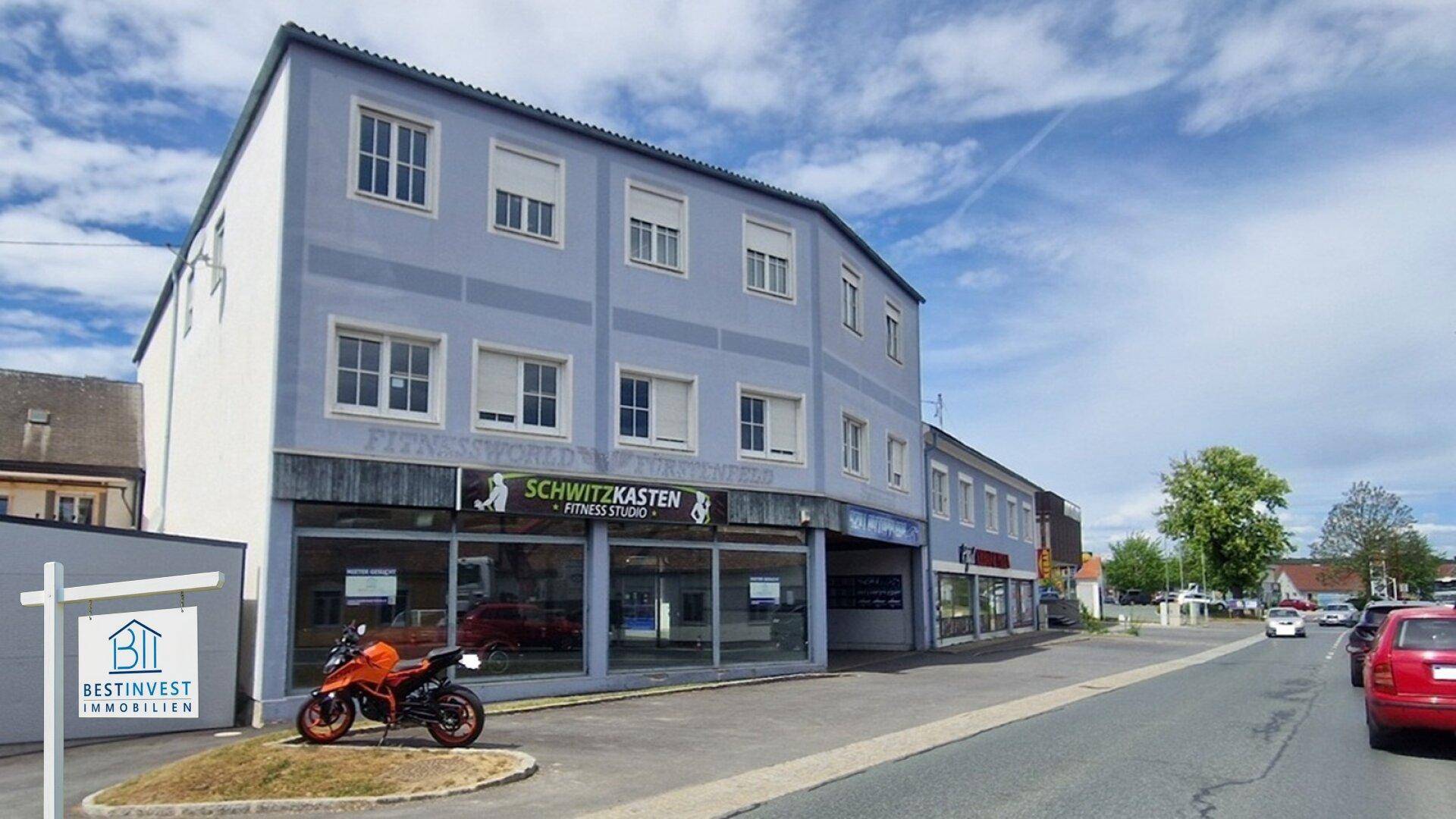 Modernes Geschäftsgebäude mit großen Schaufenstern eines Fitnessstudios, blauer Fassade und einem Motorrad davor.