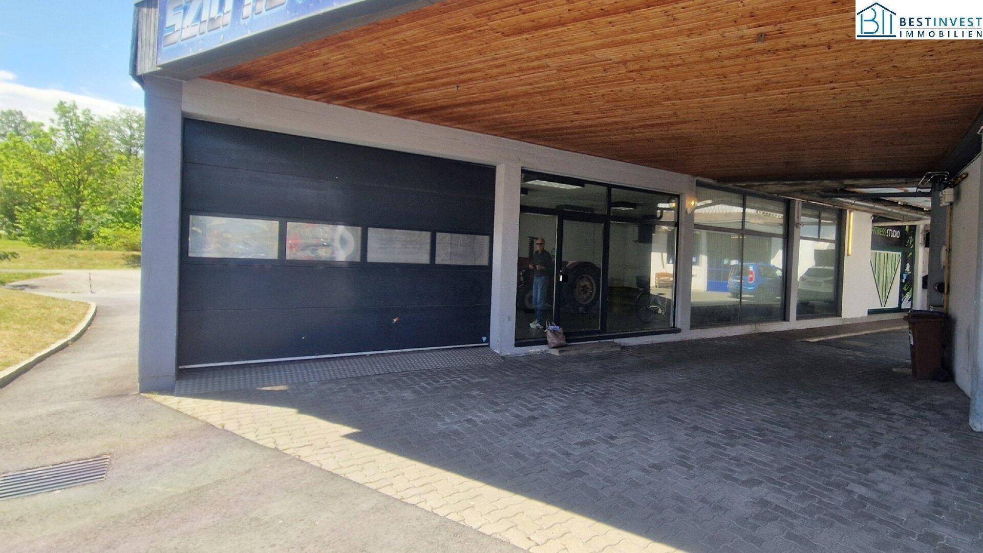Außenansicht eines Gebäudeteils mit großem schwarzen Garagentor und einem überdachten Eingangsbereich mit Holzdecke.
