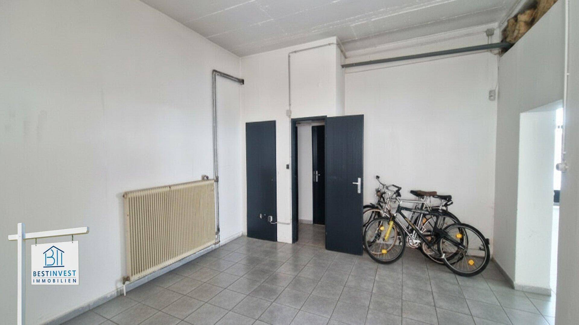 Leerer Raum mit Fliesenboden, weißen Wänden, Heizkörper und zwei Fahrrädern, die an der Wand lehnen.