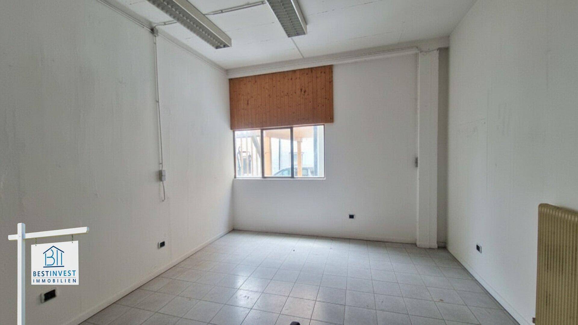 Leerer Raum mit Fliesenboden, weißen Wänden, einem Fenster mit Jalousie und einem Heizkörper.