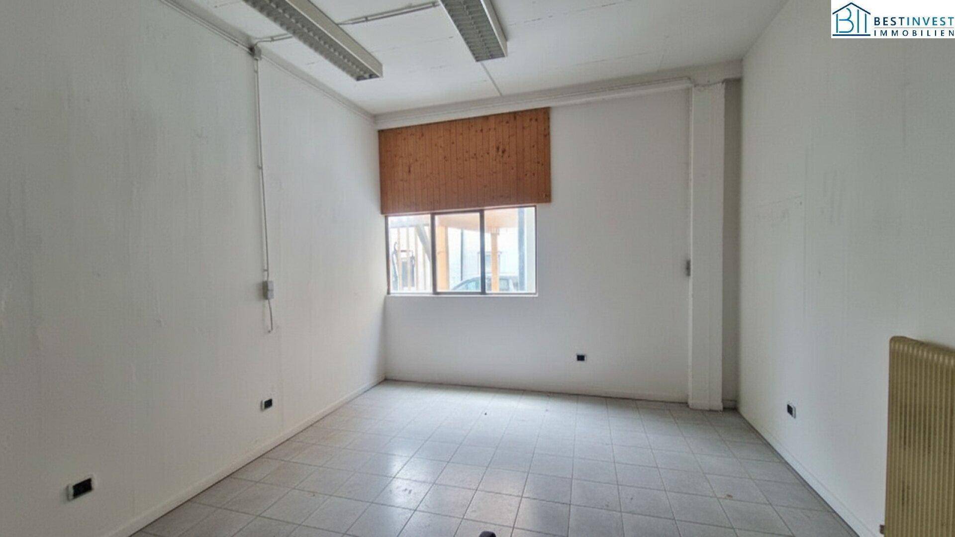 Kleiner, heller Raum mit weißen Wänden, Fliesenboden und einem Fenster mit Holzjalousie, ideal als Büro oder Lager.