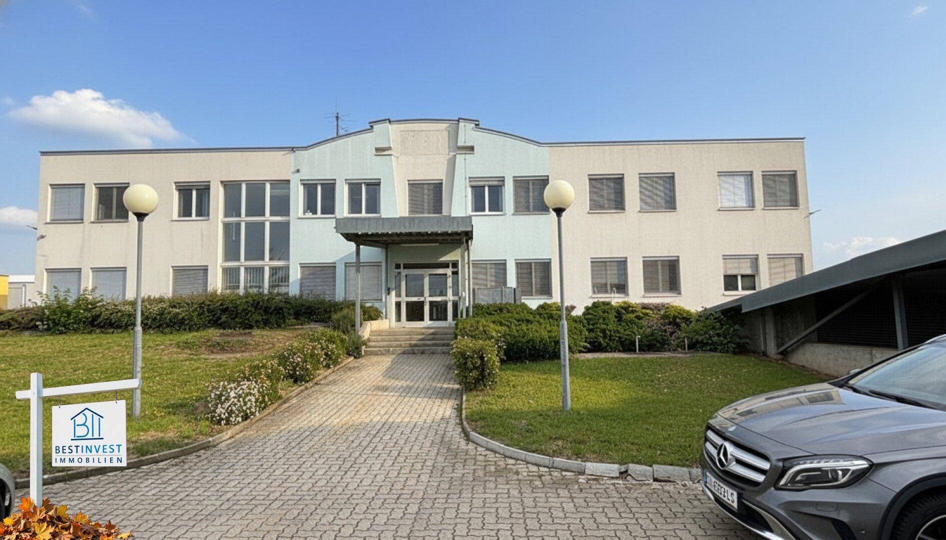 Modernes Bürogebäude mit gepflegter Grünfläche und Parkplätzen vor dem Eingang.
