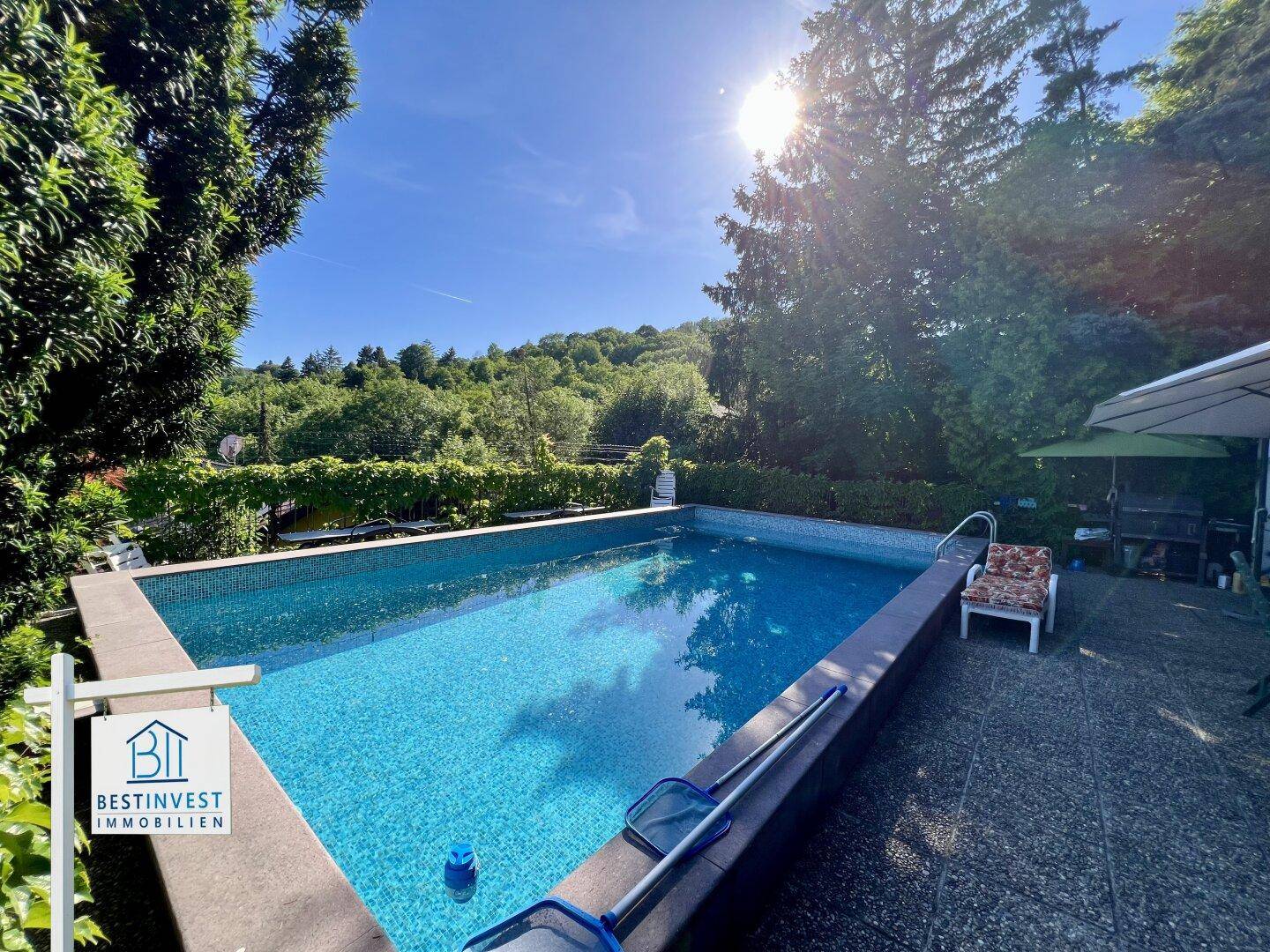Sonniger Poolbereich mit blauen Mosaikfliesen und Liegestühlen, ideal zum Entspannen im Grünen.