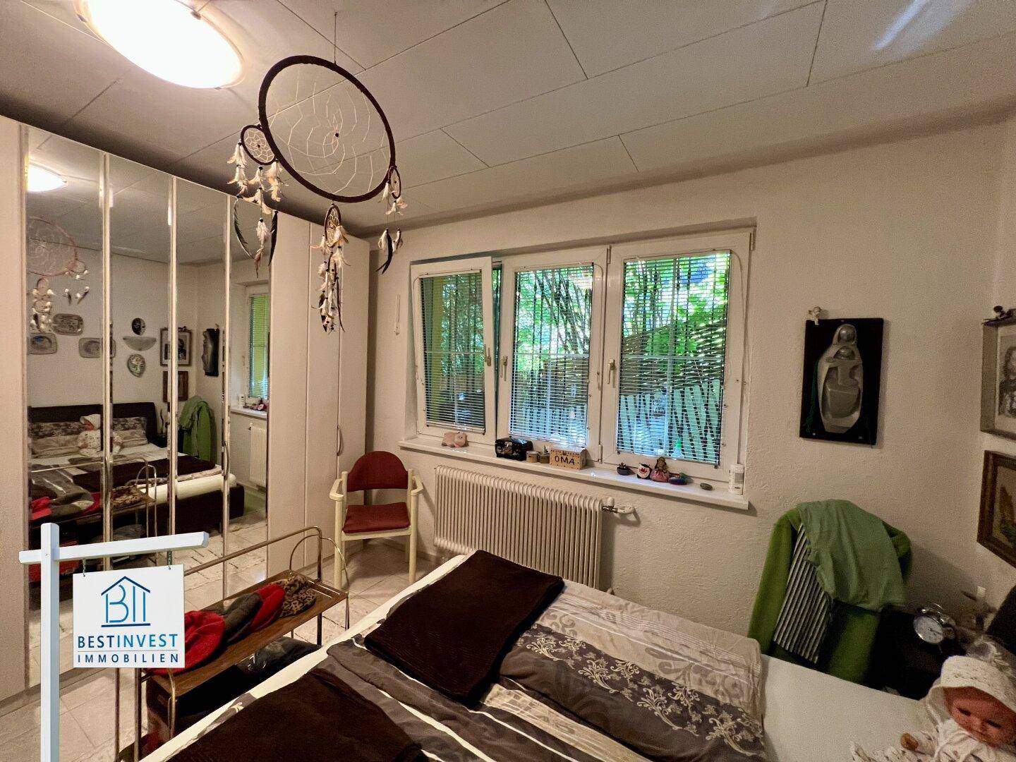 Schlafzimmer mit Fenster zum Garten, Heizkörper und praktischen Spiegelschränken.