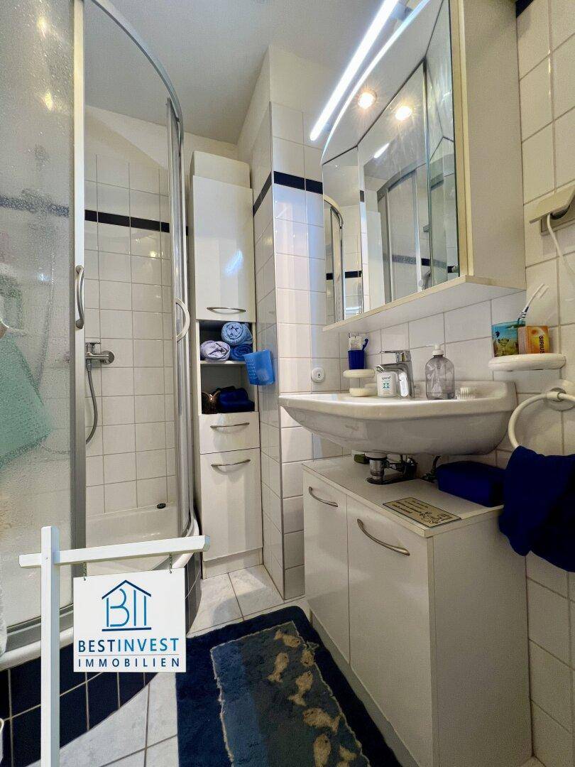 Kleines Badezimmer mit Duschkabine, Waschbecken und Spiegelschrank, funktional gefliest.