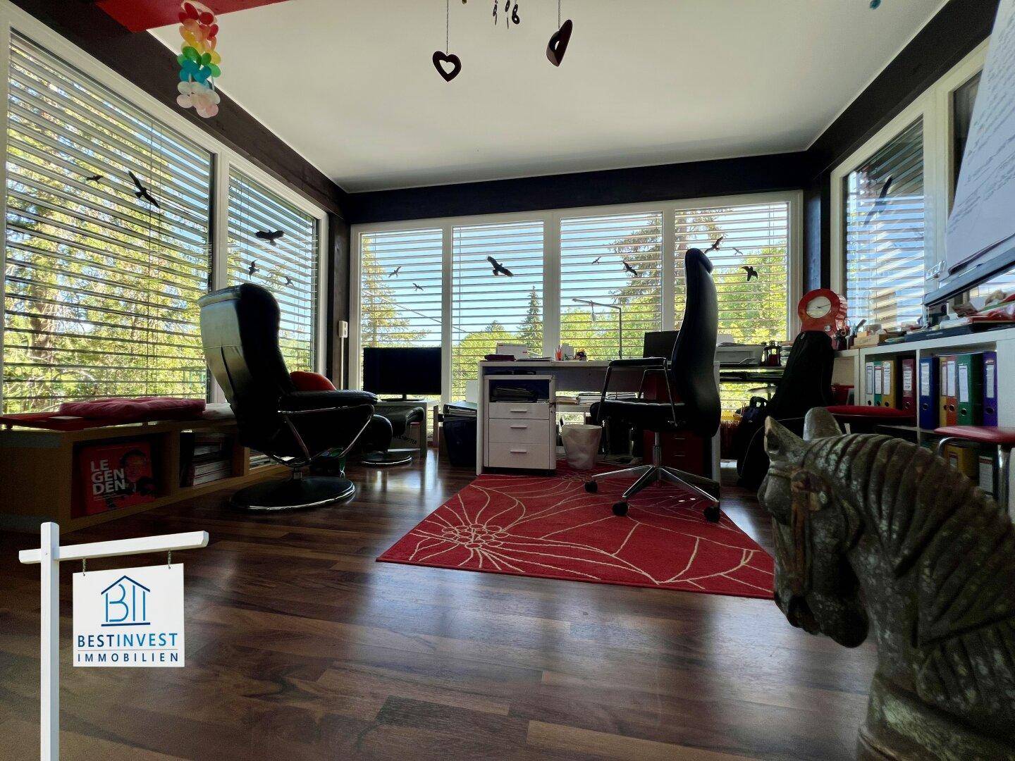 Helles Arbeitszimmer mit großen Fenstern, Holzboden und Blick ins Grüne, ausgestattet mit Büromöbeln.