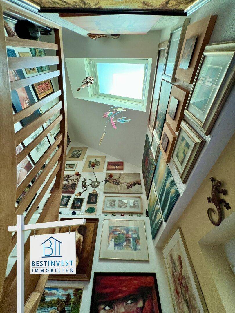 Treppenhaus mit vielen gerahmten Bildern an den Wänden und einem Oberlicht für natürliches Licht.
