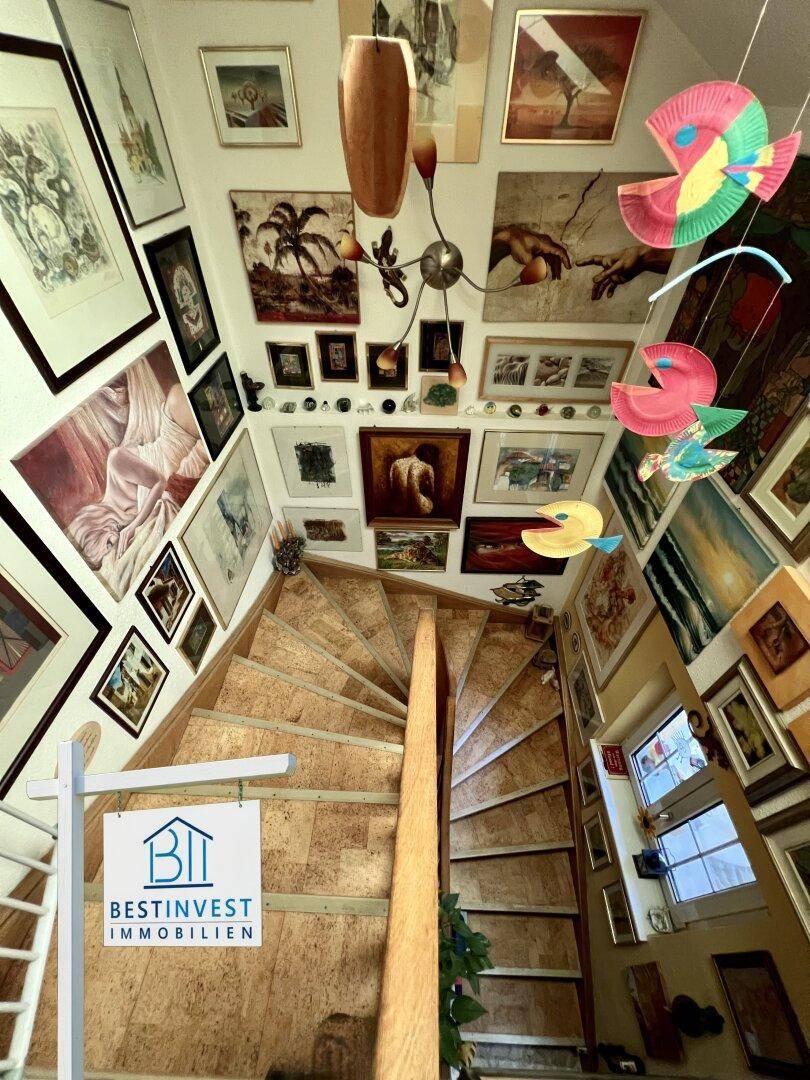 Wendeltreppe mit Holzstufen und einer Galerie von Kunstwerken, die zu den oberen Etagen führt.