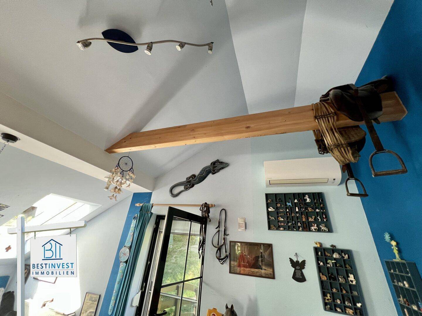 Dachschräge mit sichtbarem Holzbalken, Dachfenster und Klimaanlage in einem hellen Raum.