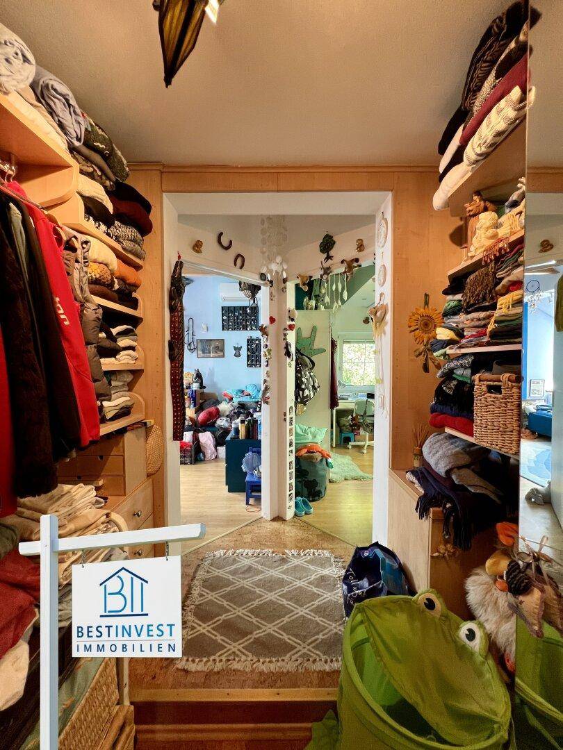 Begehbarer Kleiderschrank mit Holzregalen, der zu einem weiteren Wohnbereich führt.