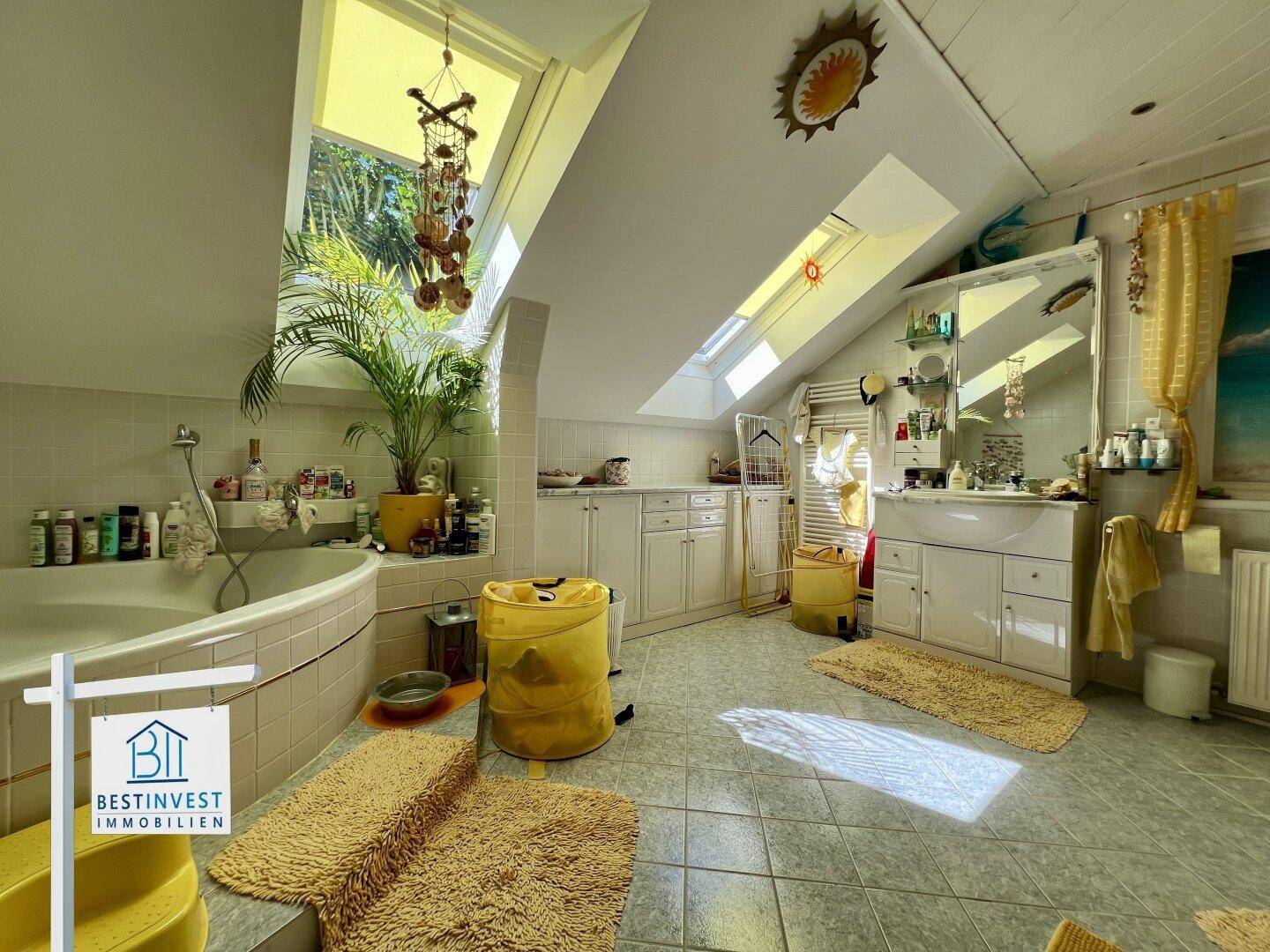 Helles Badezimmer mit großer Eckbadewanne, vielen Dachfenstern und Fliesenboden.