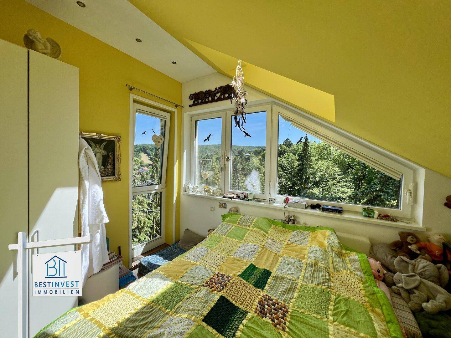 Helles Schlafzimmer im Dachgeschoss mit gelben Wänden, schrägen Decken und weitem Blick ins Grüne.