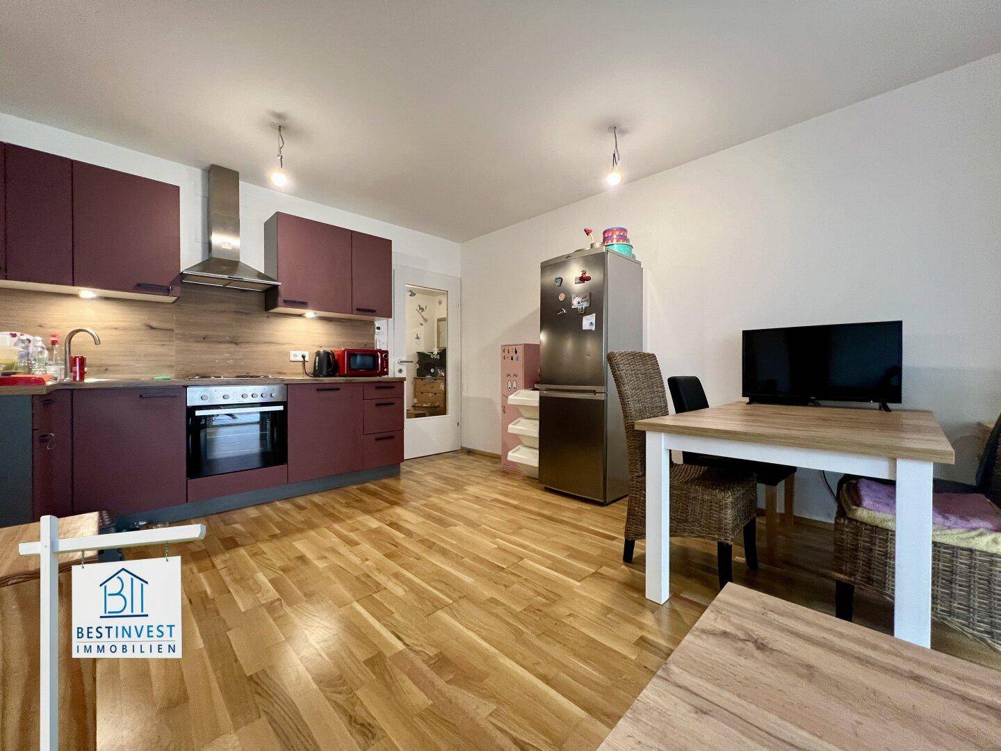 Offene Küche mit Essbereich, Holzboden und modernen weinroten Schränken.