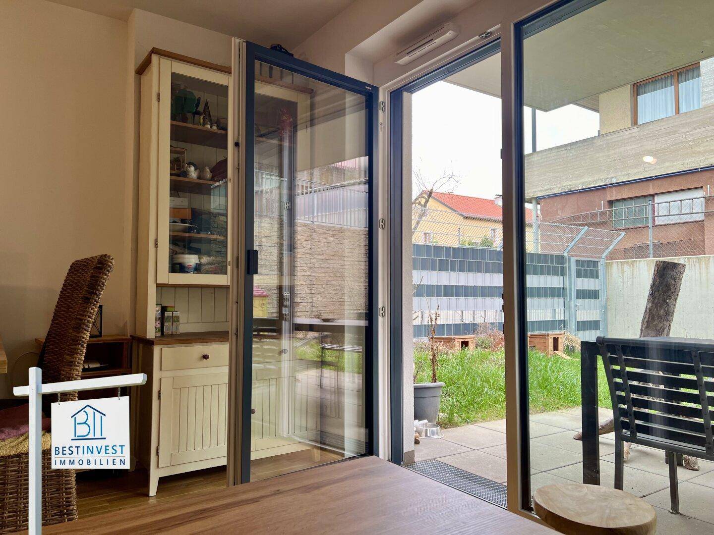 Essbereich mit großem Fenster und Zugang zu einer kleinen Grünfläche im Freien.