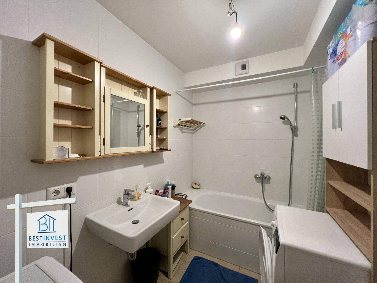Badezimmer mit Badewanne, Waschbecken und Spiegelschrank, hell gefliest.