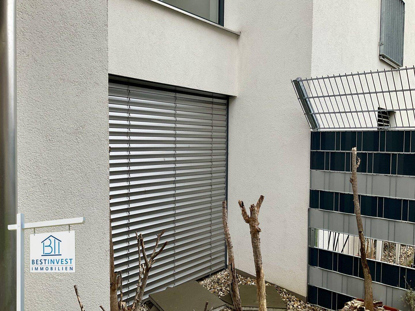 Fassadendetail mit großen Fenstern und Außenjalousien für Sonnenschutz.