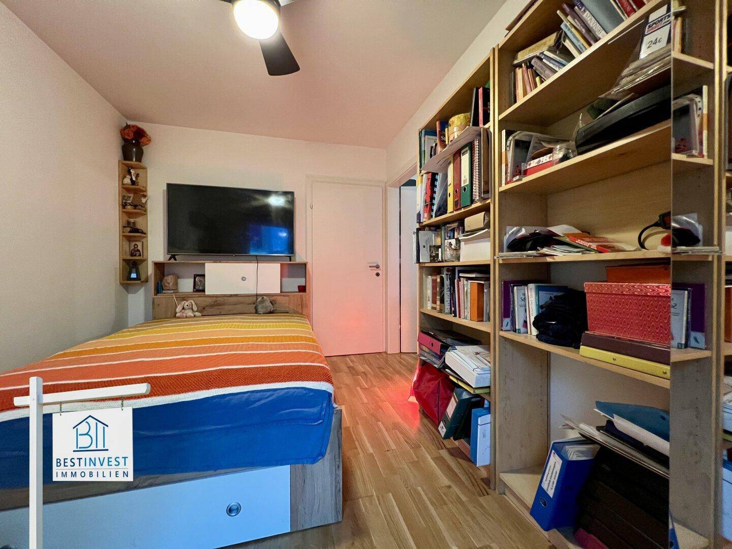 Schlafzimmer mit Holzboden, großem Bücherregal und Stauraum unter dem Bett.
