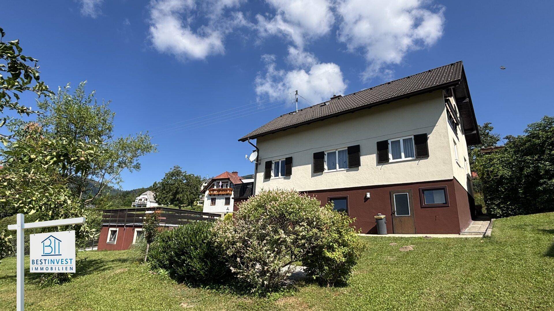 Ansicht des Hauses von vorne mit Garten und umliegender grüner Landschaft unter blauem Himmel.