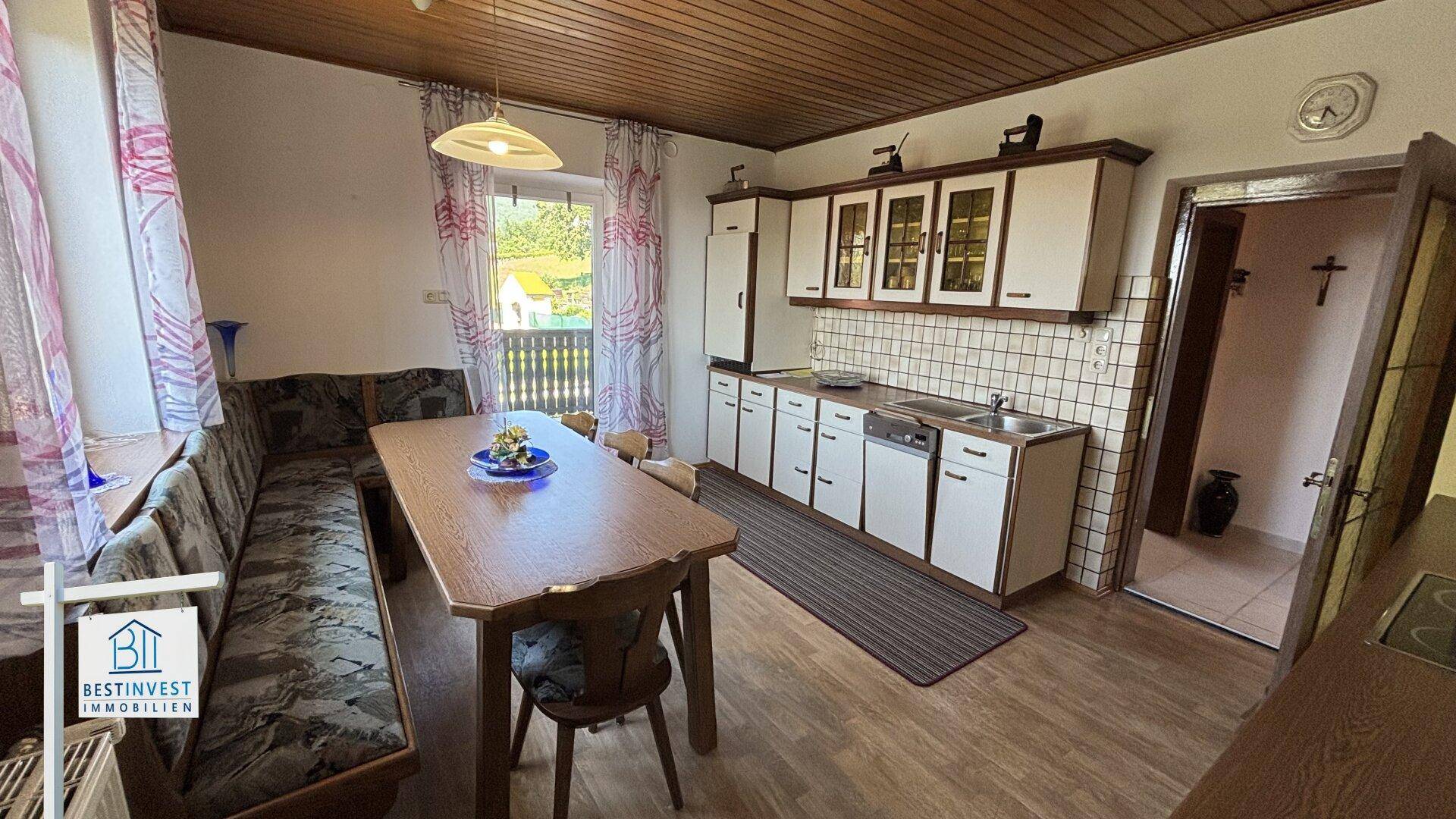 Traditionelle Küche mit Holztisch, Eckbank und Zugang zu einem kleinen Balkon.