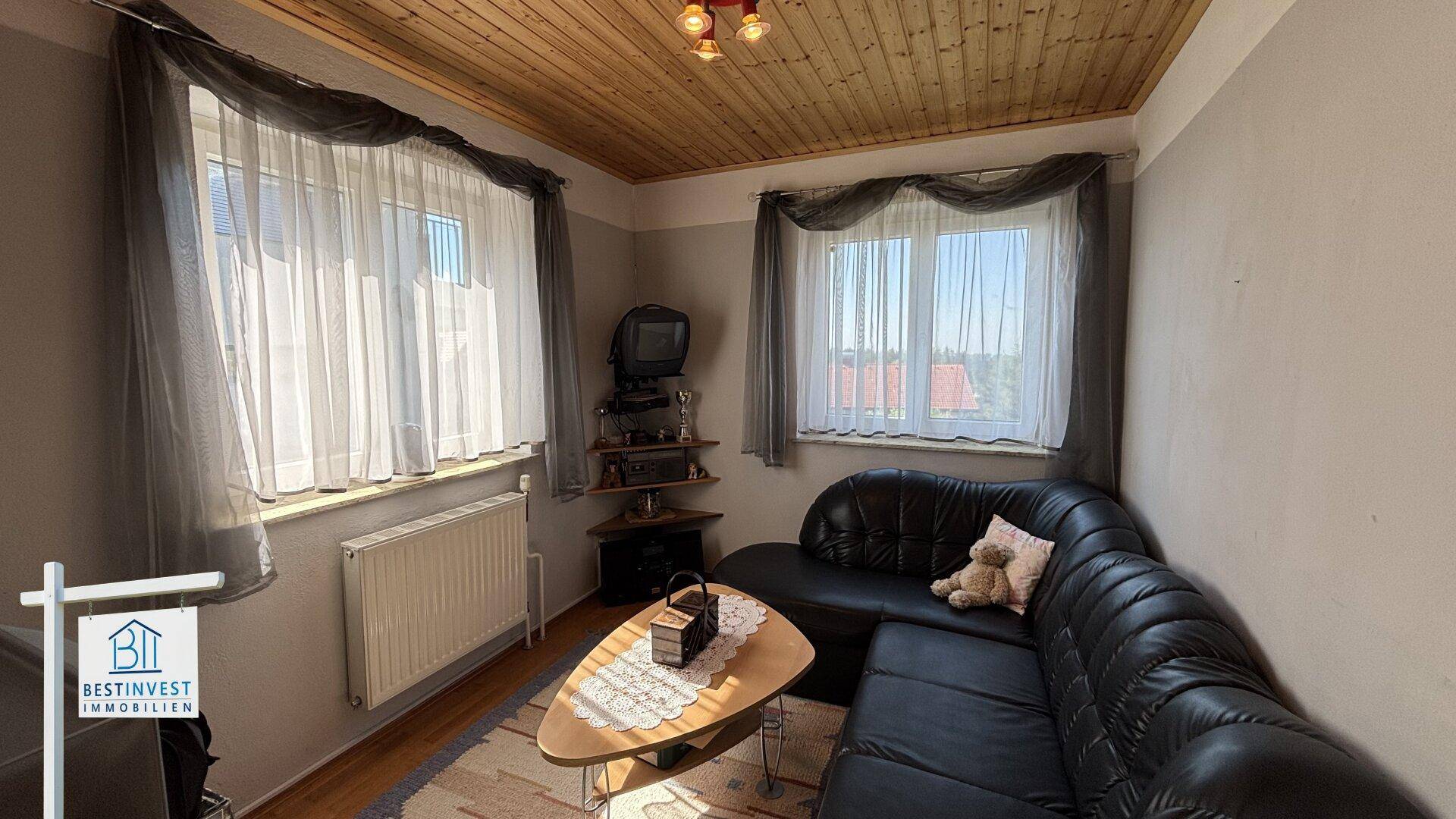 Kleines Wohnzimmer mit dunklem Ledersofa, Holztisch und Holzdecke.