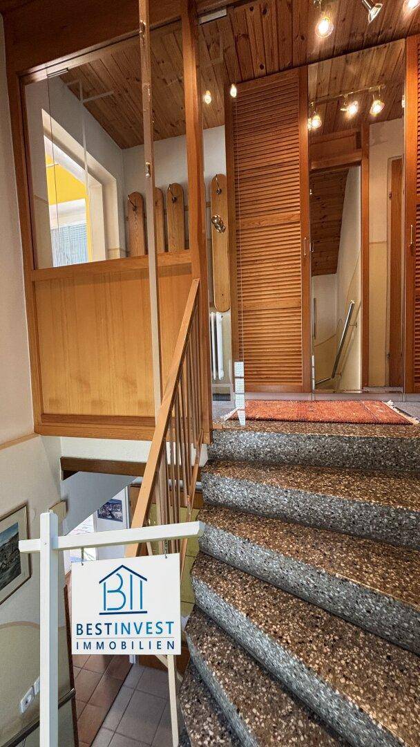 Treppenhaus mit Holzgeländer und Terrazzostufen, das die Etagen verbindet.