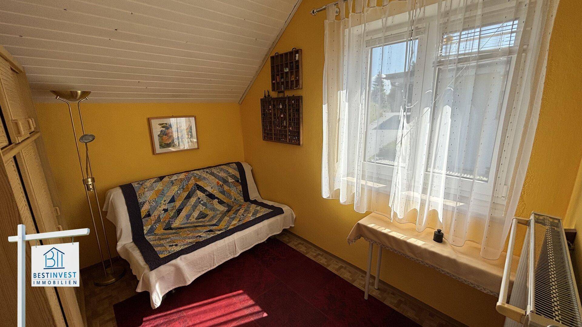 Helles Schlafzimmer mit gelben Wänden, Sofa und Fenster mit Blick ins Grüne.