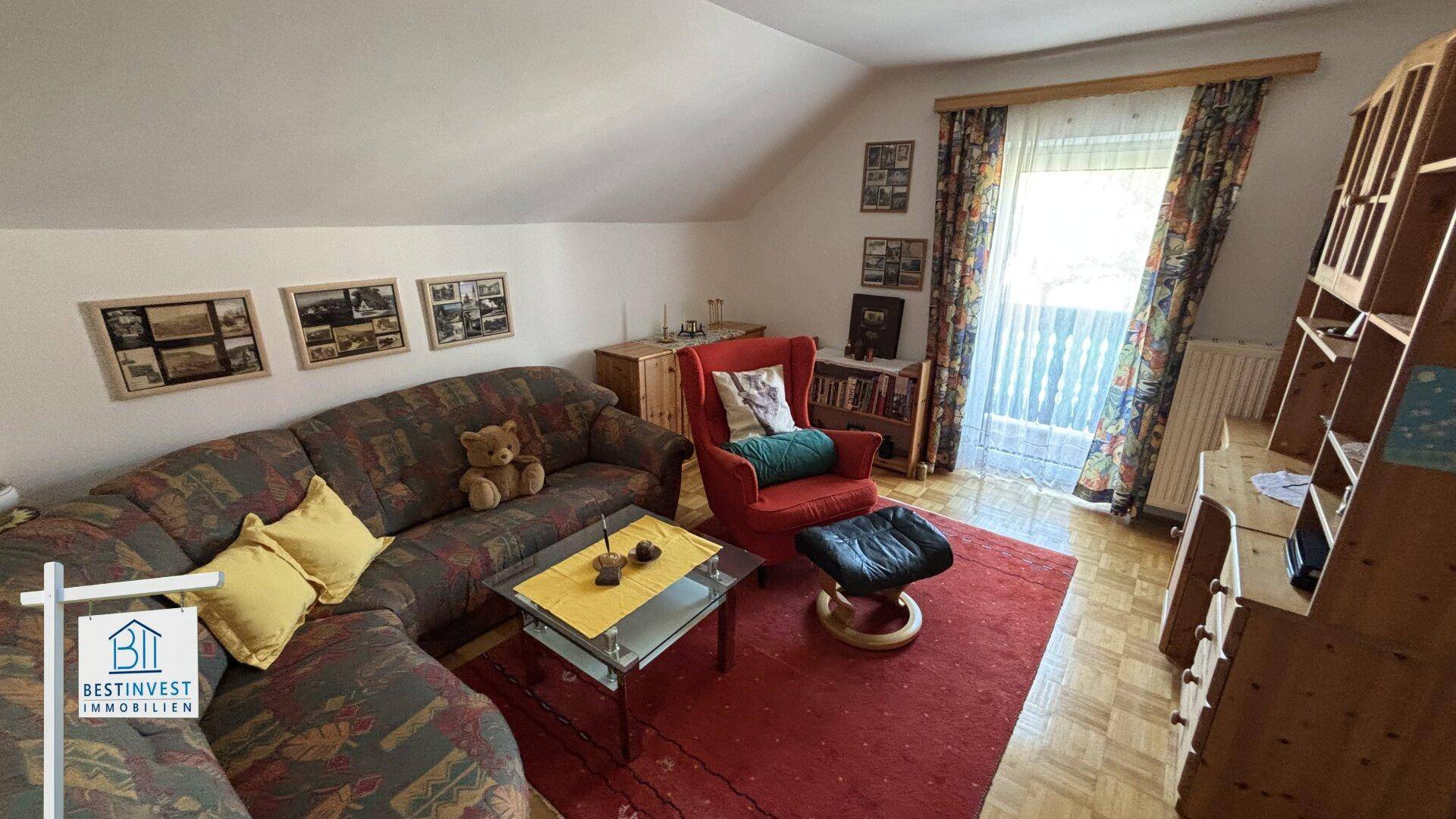 Gemütliches Wohnzimmer im Dachgeschoss mit Sofa, Sessel und Balkonzugang.