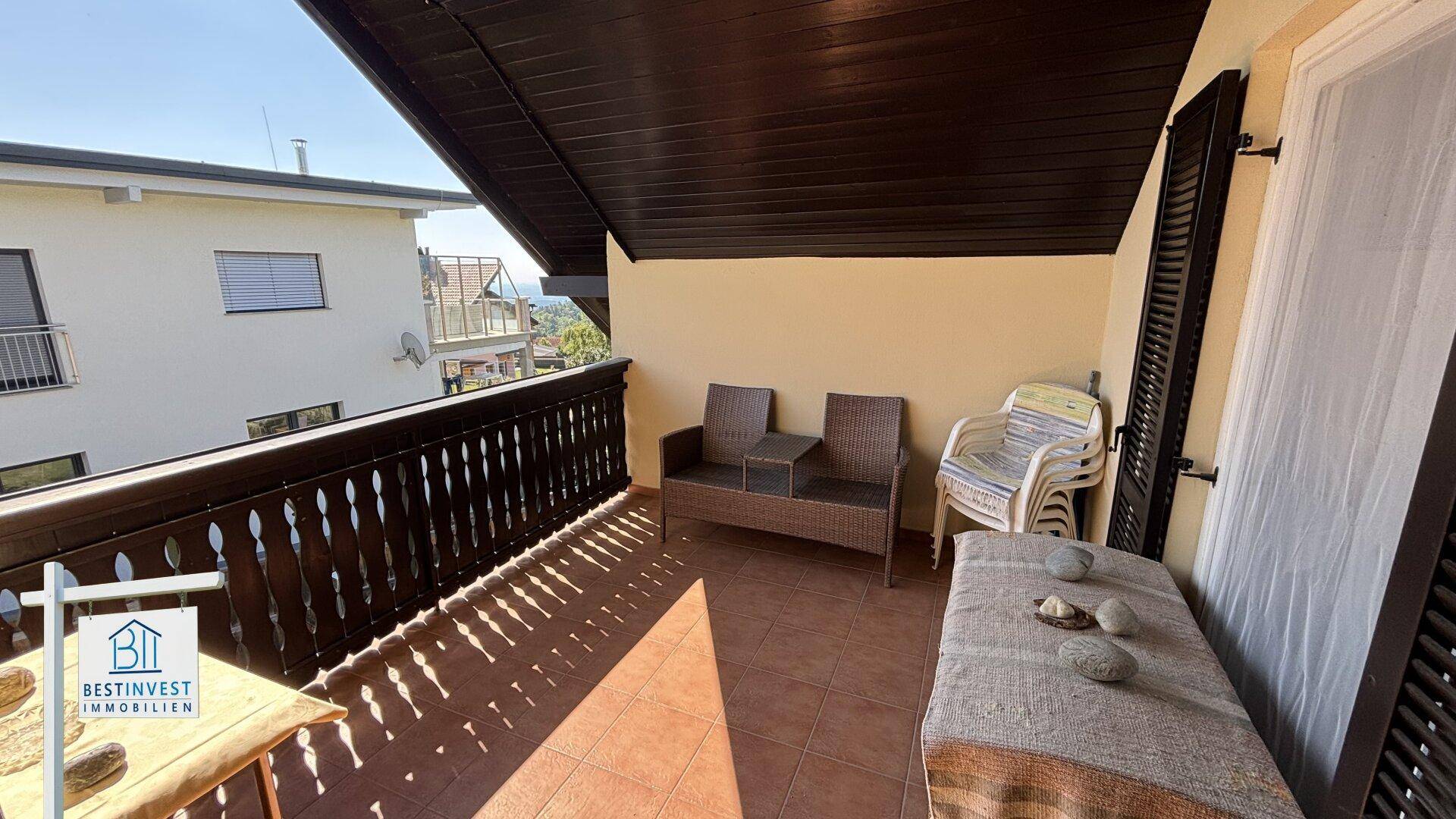 Überdachter Balkon mit Sitzgelegenheiten und Blick auf die umliegenden Häuser und Berge.