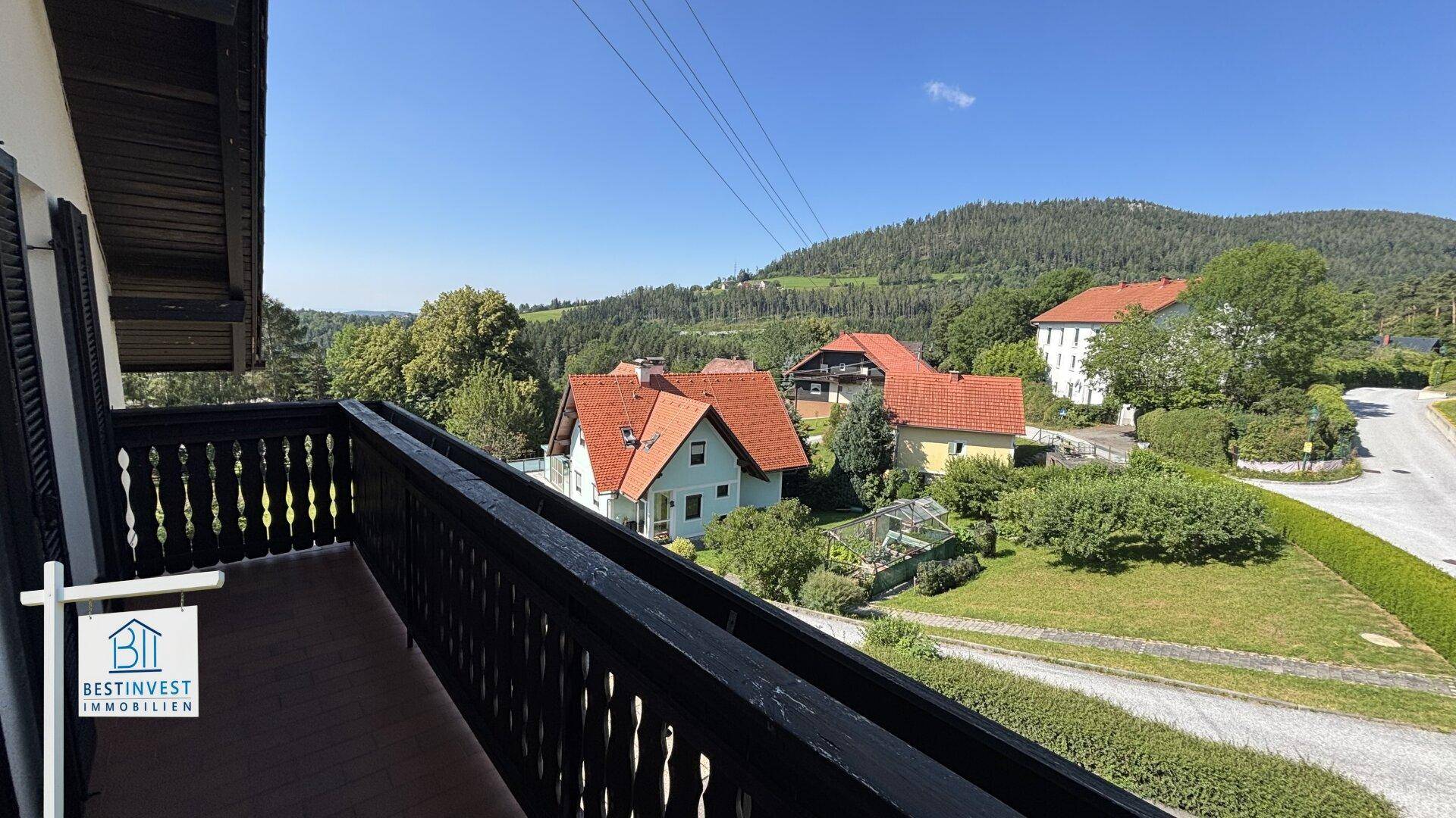 Langer Balkon mit Holzgeländer und weitem Blick über die Landschaft und Dächer.
