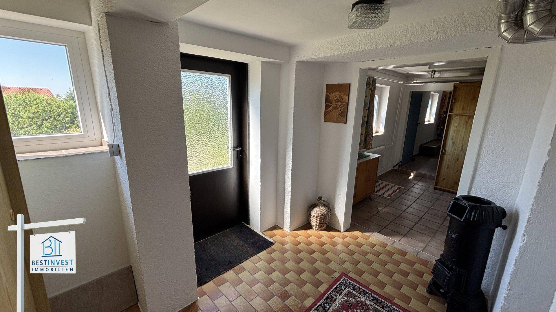 Heller Eingangsbereich mit Fliesenboden, Holzofen und Zugang zu weiteren Räumen.