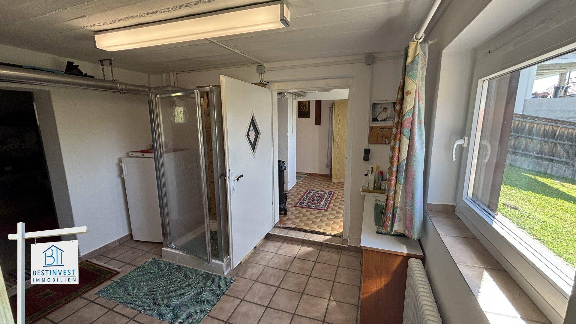 Praktischer Raum mit Duschkabine, Fliesenboden und Fenster zum Garten.