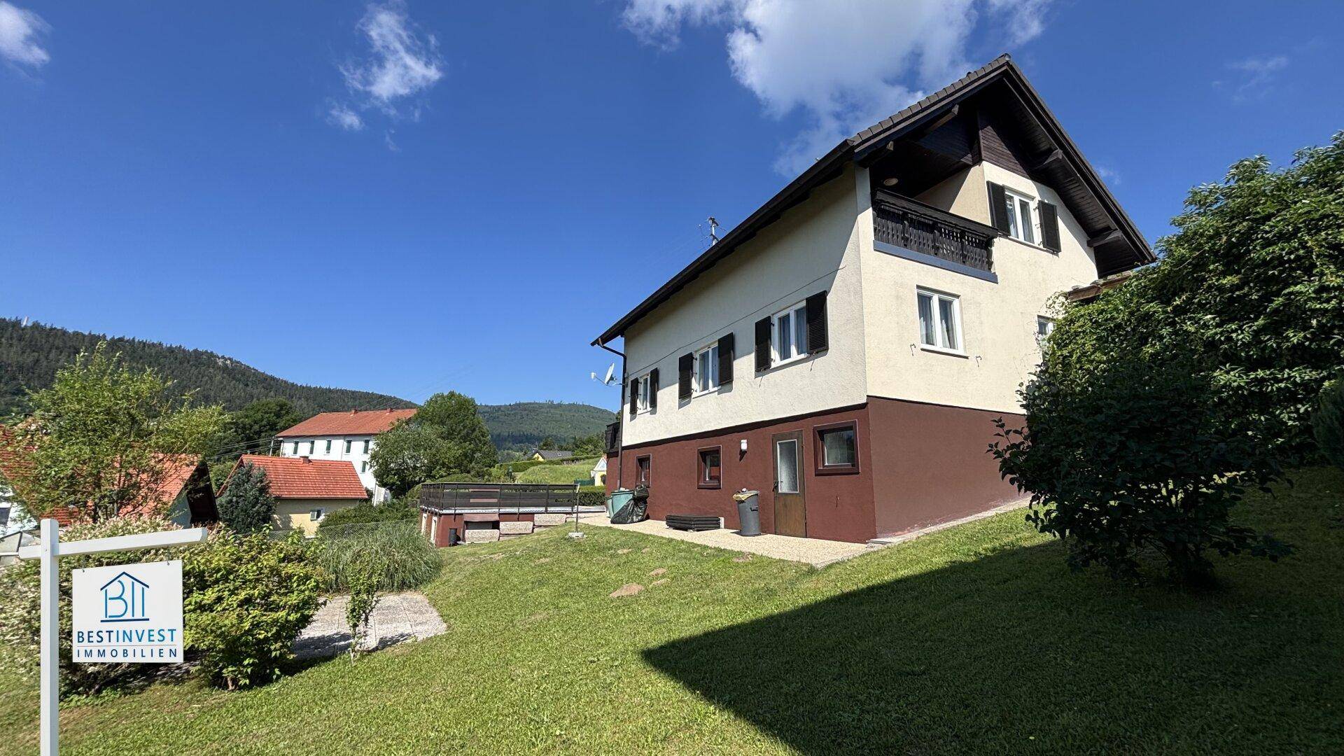 Ansicht des Hauses von der Seite mit Garten und umliegender grüner Landschaft unter blauem Himmel.