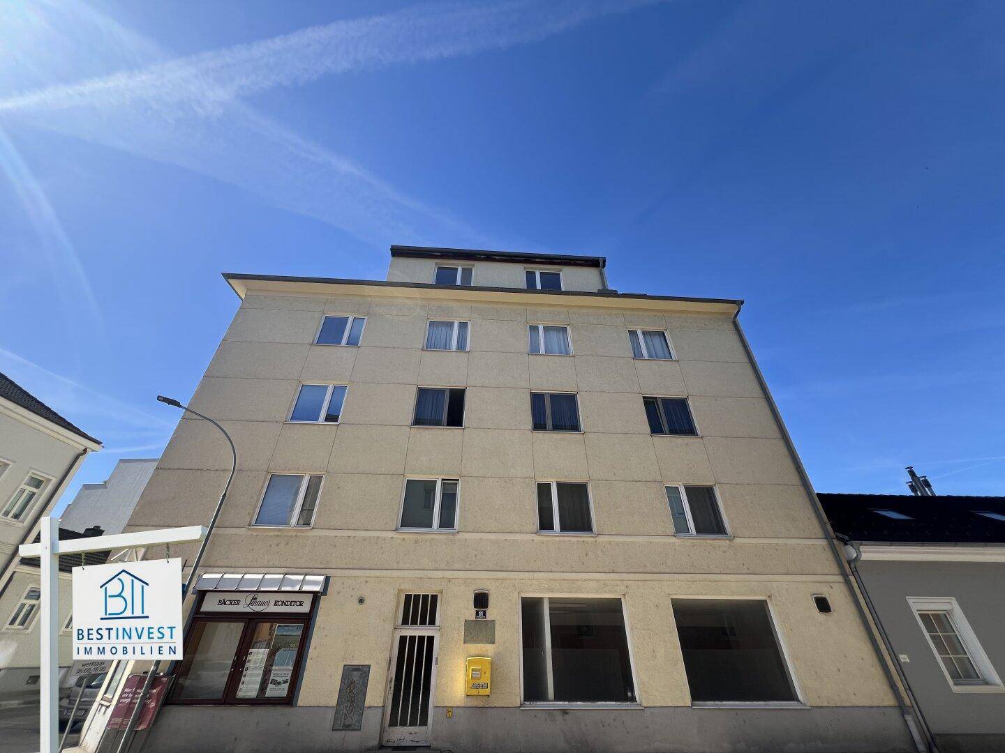 Vorderansicht eines mehrstöckigen Wohnhauses mit Geschäften im Erdgeschoss und gelber Fassade.