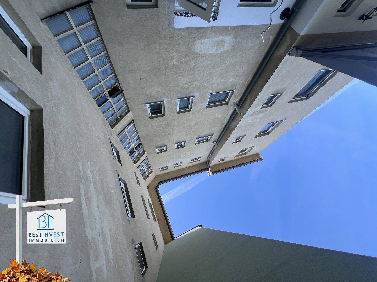 Vertikale Ansicht eines Innenhofs mit mehreren Fensterreihen und klarem blauem Himmel.