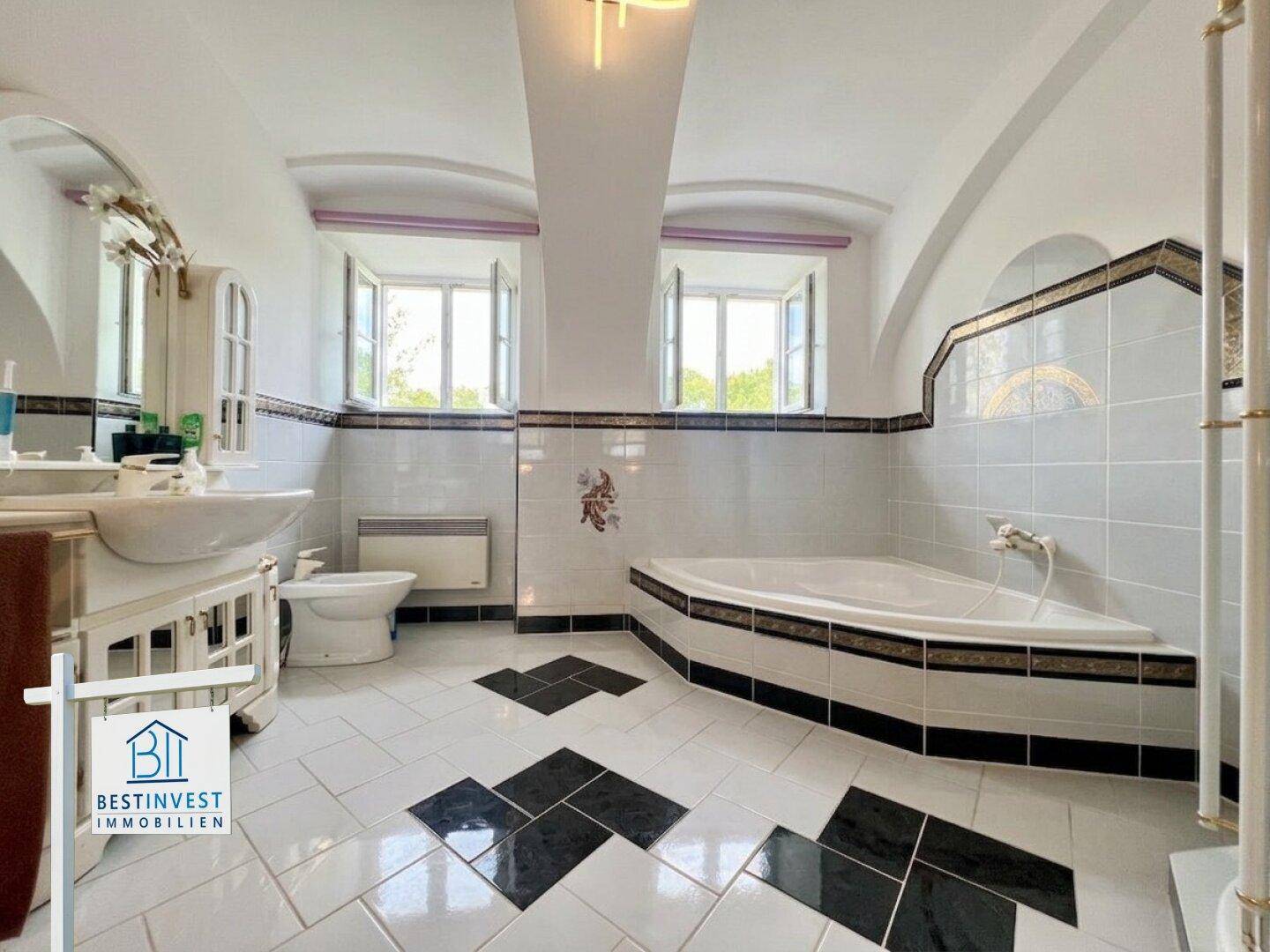 Geräumiges Badezimmer mit Eckbadewanne, Waschbecken, WC und dekorativen Fliesen an Wänden und Boden.