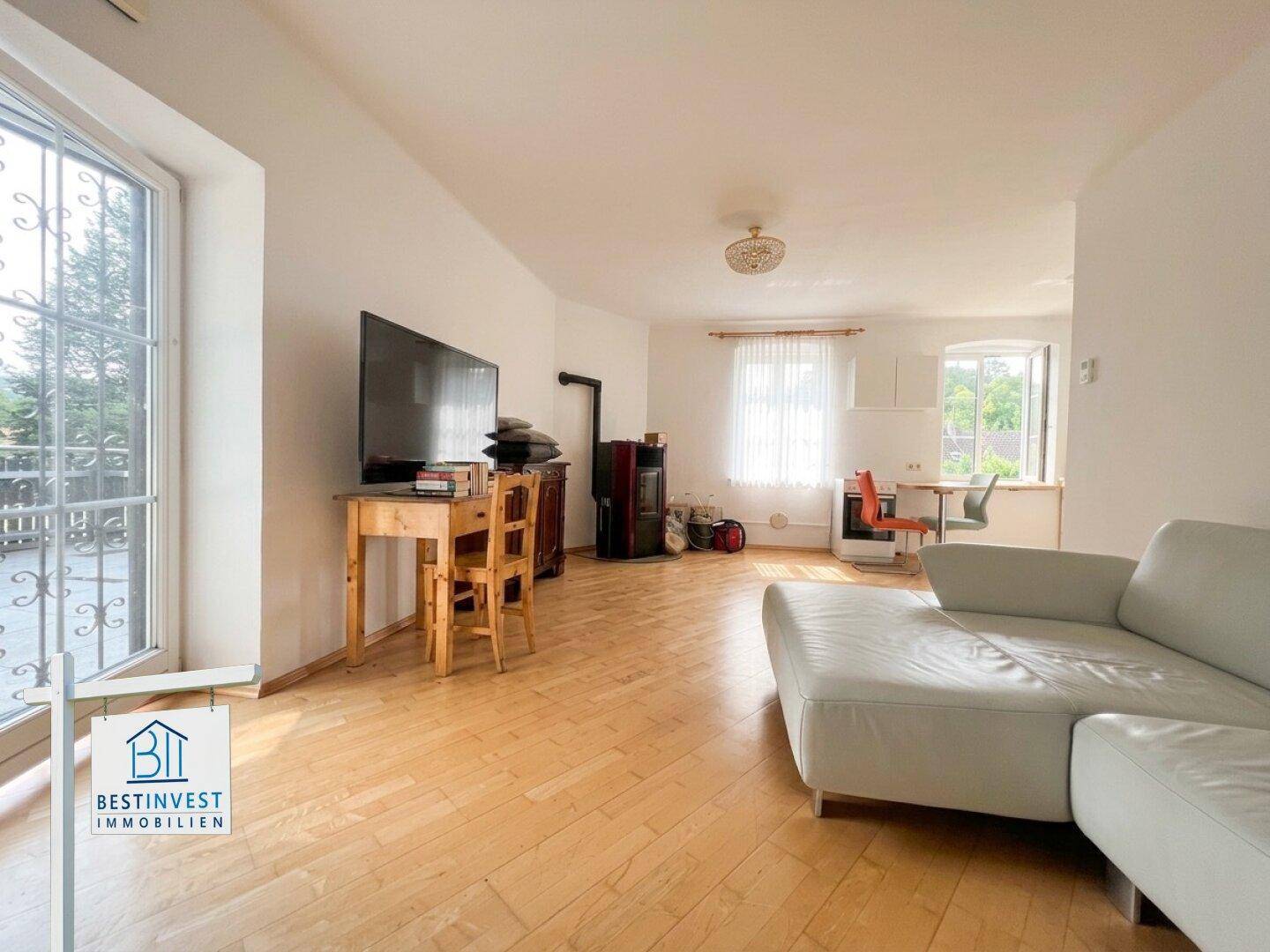 Helles Wohnzimmer mit Sofa, Fernseher, Holzofen und Holzdielenboden.
